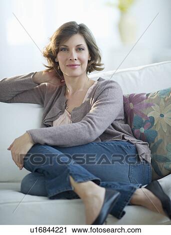 Stock Image - Portrait of woman sitting on sofa. Fotosearch