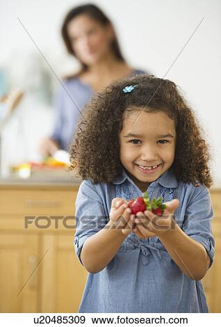 Smiling girl (6-7) holding strawberries with defocused woman in background View Large Photo Image Stock Photo - Smiling girl (6-7) holding strawberries with defocused woman in background. Fotosearch
