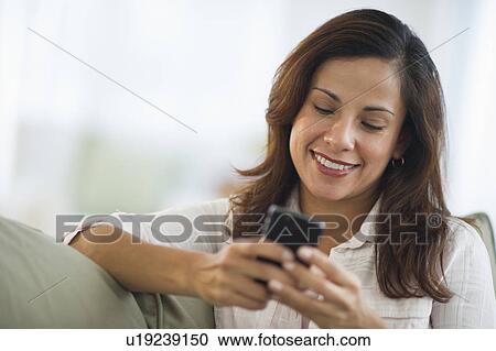 Stock Image - Smiling woman sitting texting on mobile phone. Fotosearch