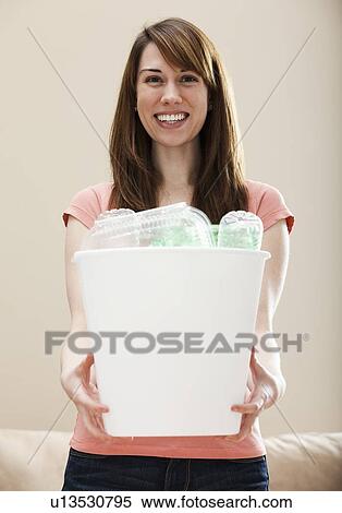 Stock Photography - Studio portrait of smiling woman holding recycling bin in plastic bottle. Fotosearch