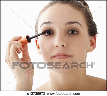 Stock Image - Studio portrait of young woman applying mascara. Fotosearch