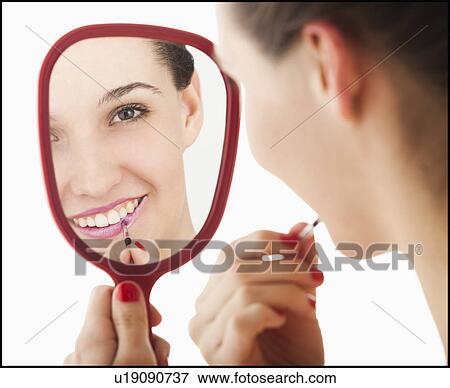 Stock Photo - Studio portrait of young woman applying lipstick in mirror. Fotosearch