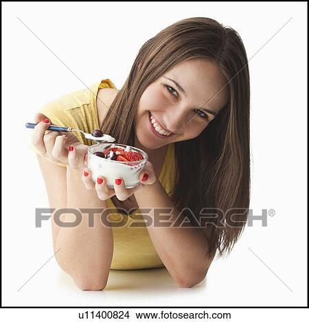 Picture - Studio portrait of young woman eating strawberries and yogurt. Fotosearch