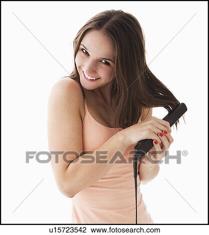 Stock Image - Studio portrait of young woman straightening hair. Fotosearch