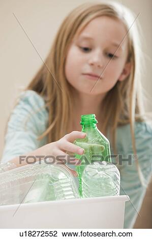 Stock Image - Studio shot of girl (8-9) placing plastic bottle in recycling bin. Fotosearch