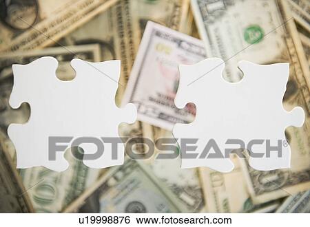 Stock Photograph - Studio shot of jigsaw pieces against heap of money. Fotosearch