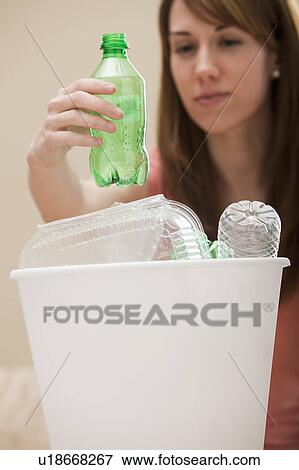 Stock Photo - Studio shot of woman (8-9) placing plastic bottle in recycling bin. Fotosearch