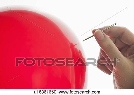 Stock Image - Studio shot of woman holding needle close to red balloon. Fotosearch