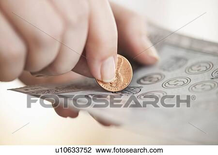 Stock Image - Studio shot of woman scratching lottery ticket. Fotosearch