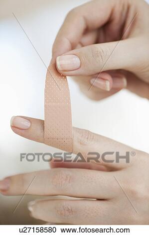 Stock Image - Studio shot of woman sticking adhesive bandage on finger. Fotosearch