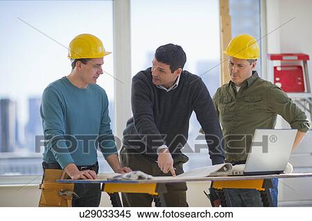 Stock Photography - Three man reading blueprint and using laptop on construction site. Fotosearch