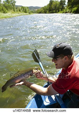 Stock Photo - USA, Colorado, Man sitting in fishing boat, holding large trout. Fotosearch