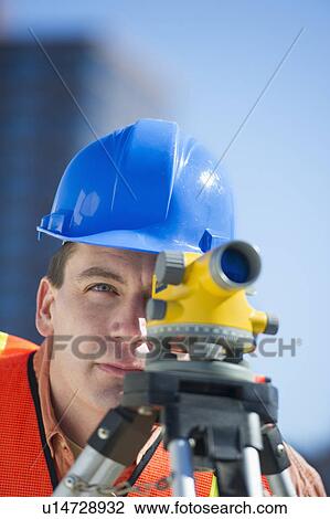 Stock Image - USA, New Jersey, Jersey City, construction worker in hard hat using theodolite. Fotosearch