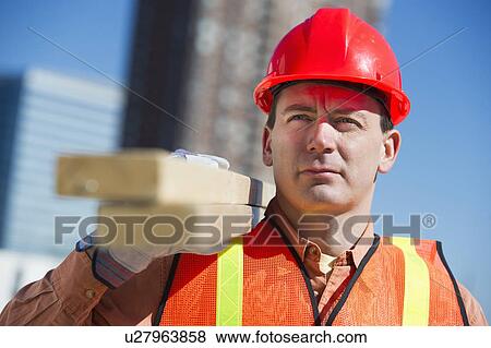 Stock Photo - USA, New Jersey, Jersey City, construction worker carrying planks. Fotosearch