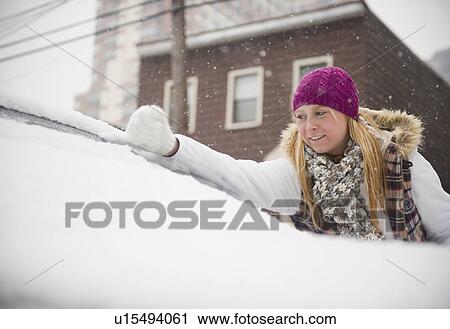 Stock Image - USA, New Jersey, Jersey City, woman removing snow from wind shield. Fotosearch