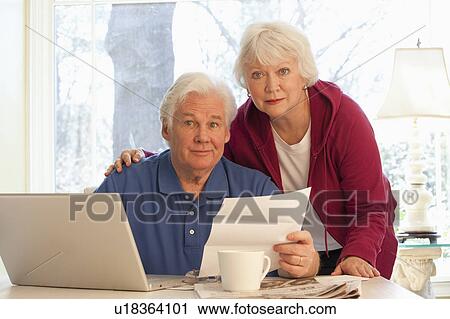 Stock Image - USA, Virginia, Richmond, portrait of senior couple paying bills with laptop. Fotosearch