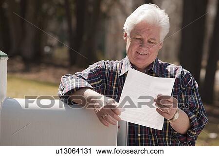 Stock Image - USA, Virginia, Richmond, senior man reading letter by mailbox. Fotosearch