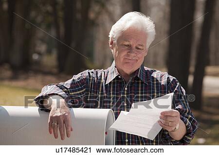 Stock Image - USA, Virginia, Richmond, senior man reading letter by mailbox. Fotosearch