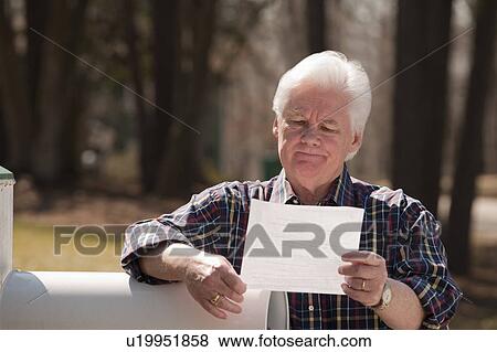 Stock Photo - USA, Virginia, Richmond, senior man reading letter by mailbox. Fotosearch