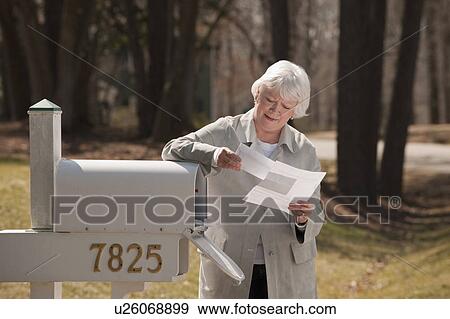 Stock Photo - USA, Virginia, Richmond, senior woman reading letters by mailbox. Fotosearch
