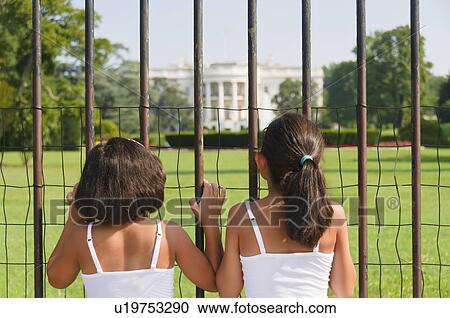 Stock Image - USA, Washington DC, two girls looking at White House through fence. Fotosearch