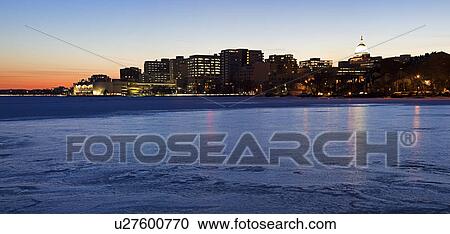 Stock Image - USA, Wisconsin, Madison skyline across frozen lake at dusk. Fotosearch