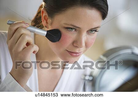 Stock Image - Woman applying blush on cheekbones. Fotosearch