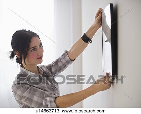 Stock Image - Woman hanging picture on wall. Fotosearch