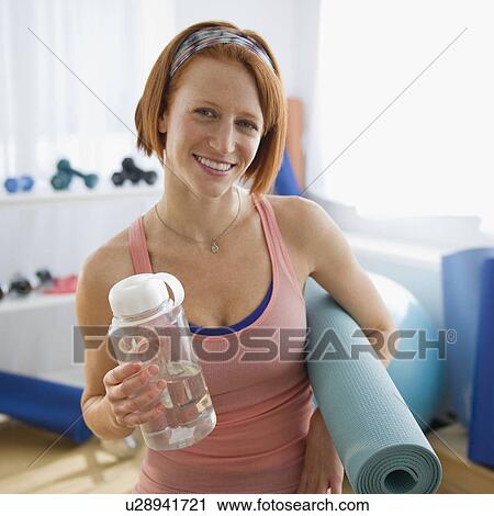 Stock Image - Woman holding exercise mat and bottle water. Fotosearch