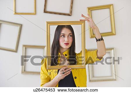 Stock Image - Woman holding picture frame over face. Fotosearch