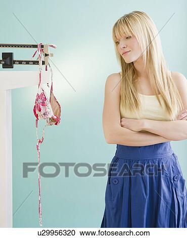 Stock Image - Woman looking at bikini hanging on weight scale. Fotosearch