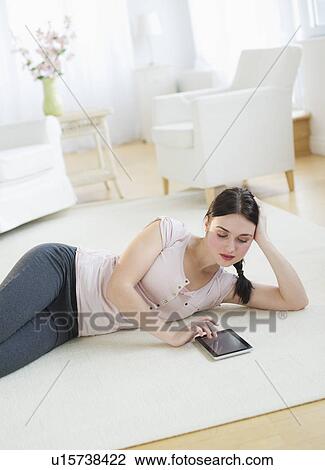 Stock Image - Woman lying on floor and using tablet. Fotosearch
