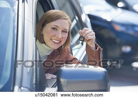 Stock Image - Woman sitting in new car showing car key. Fotosearch