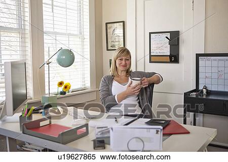 Woman sitting in office room, holding cup of tea View Large Photo Image Stock Photography - Woman sitting in office room, holding cup of tea. Fotosearch