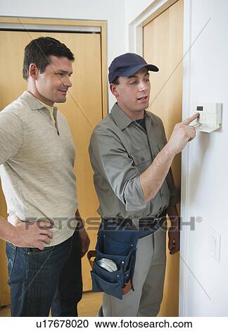 Stock Image - Worker and house owner setting up security system. Fotosearch