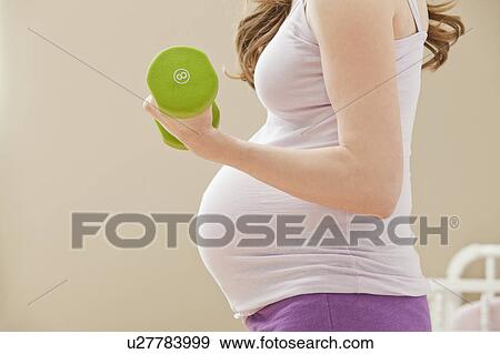 Stock Photo - Young pregnant woman excercising with dumbbells. Fotosearch
