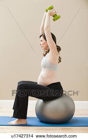 Young pregnant woman exercising with dumbbells and fitness ball View Large Photo Image Picture - Young pregnant woman exercising with dumbbells and fitness ball. Fotosearch