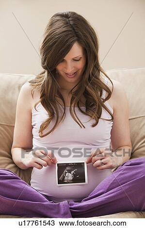 Stock Image - Young pregnant woman looking at CT image of unborn baby. Fotosearch