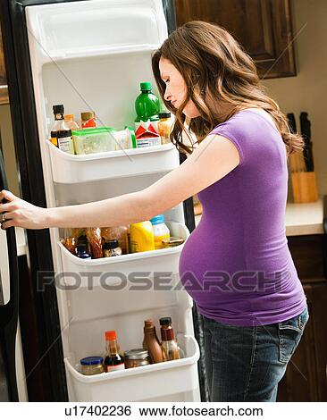Stock Photograph - Young pregnant woman looking at inside of fridge . Fotosearch