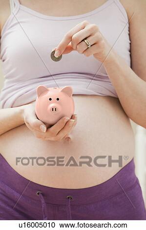 Young pregnant woman putting coin into pink piggybank View Large Photo Image Stock Image - Young pregnant woman putting coin into pink piggybank. Fotosearch