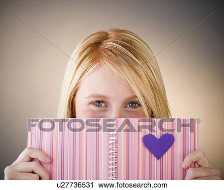 Stock Image - Young woman hiding behind diary. Fotosearch