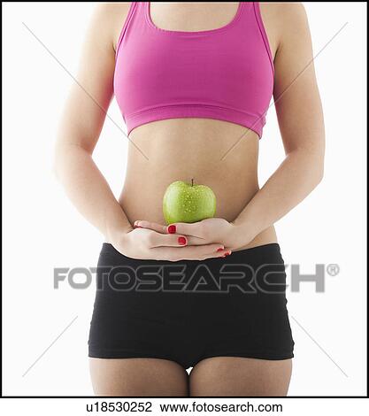 Stock Image - Young woman holding apple against belly. Fotosearch