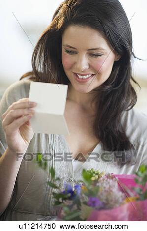 Stock Image - Young woman holding bouquet and reading greeting card. Fotosearch
