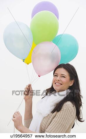 Stock Photo - Young woman holding bunch of balloons smiling. Fotosearch
