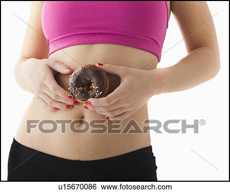 Stock Photograph - Young woman holding doughnut against belly. Fotosearch