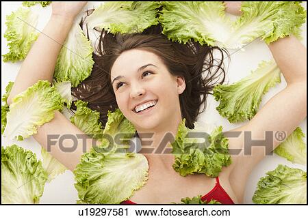 Stock Image - Young woman lying in lettuce leaves. Fotosearch