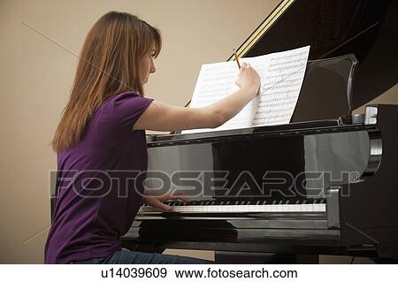 Stock Photo - Young woman marking score before setting to play grand piano. Fotosearch