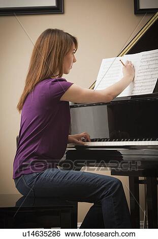 Stock Photograph - Young woman marking score before setting to play grand piano. Fotosearch