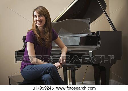 Stock Photography - Young woman sitting by grand piano, smiling. Fotosearch
