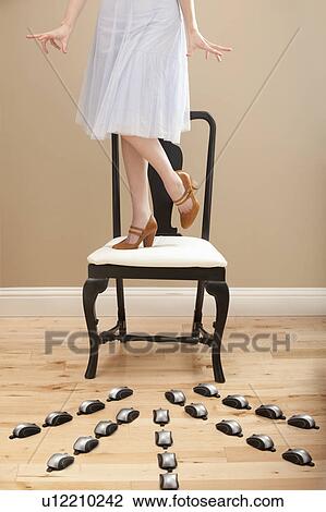 Young woman standing on chair, evading computer mice View Large Photo Image Stock Image - Young woman standing on chair, evading computer mice. Fotosearch